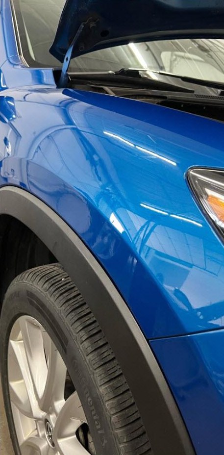 Parafango dell'auto blu dopo aver tolto l'ammaccatura con tecnica PDR, senza verniciare