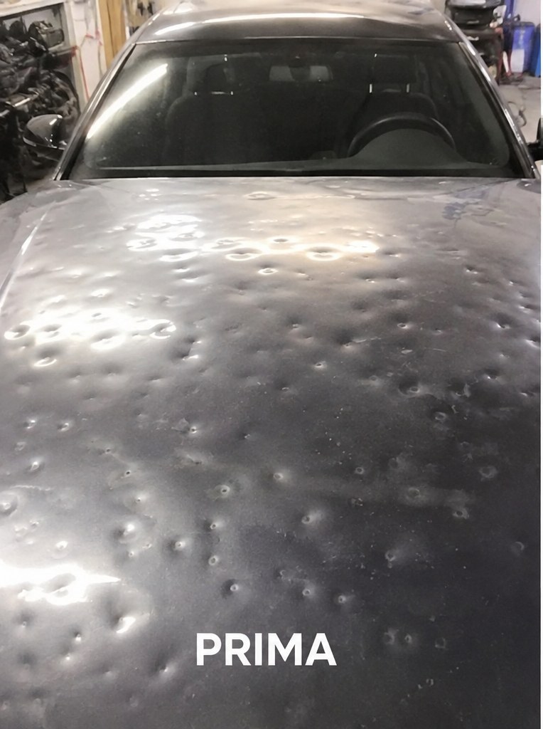 Cofano di un'auto grigia coperto di bolli da grandine prima della riparazione