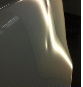 Fiancata di auto chiara con ammaccatura evidenziata dalla luce prima del levabolli