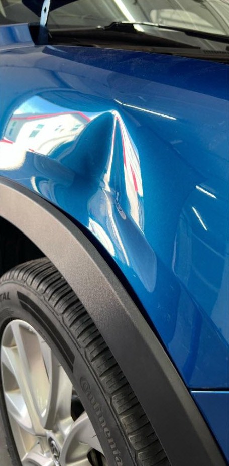 Ammaccatura profonda sul parafango di un'auto blu prima della riparazione PDR